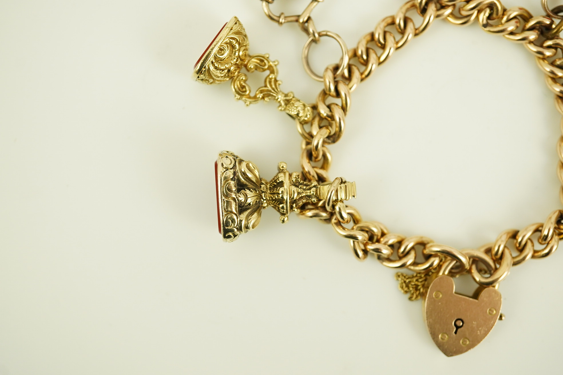 An Edwardian 15ct gold curb link charm bracelet with heart shaped padlock clasp, hung with six assorted gold overlaid and carnelian set fob seals